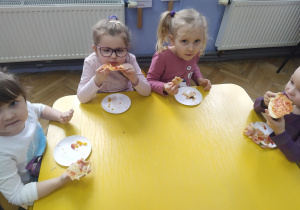 Dzieci jedzą pizzę przy stoliku.